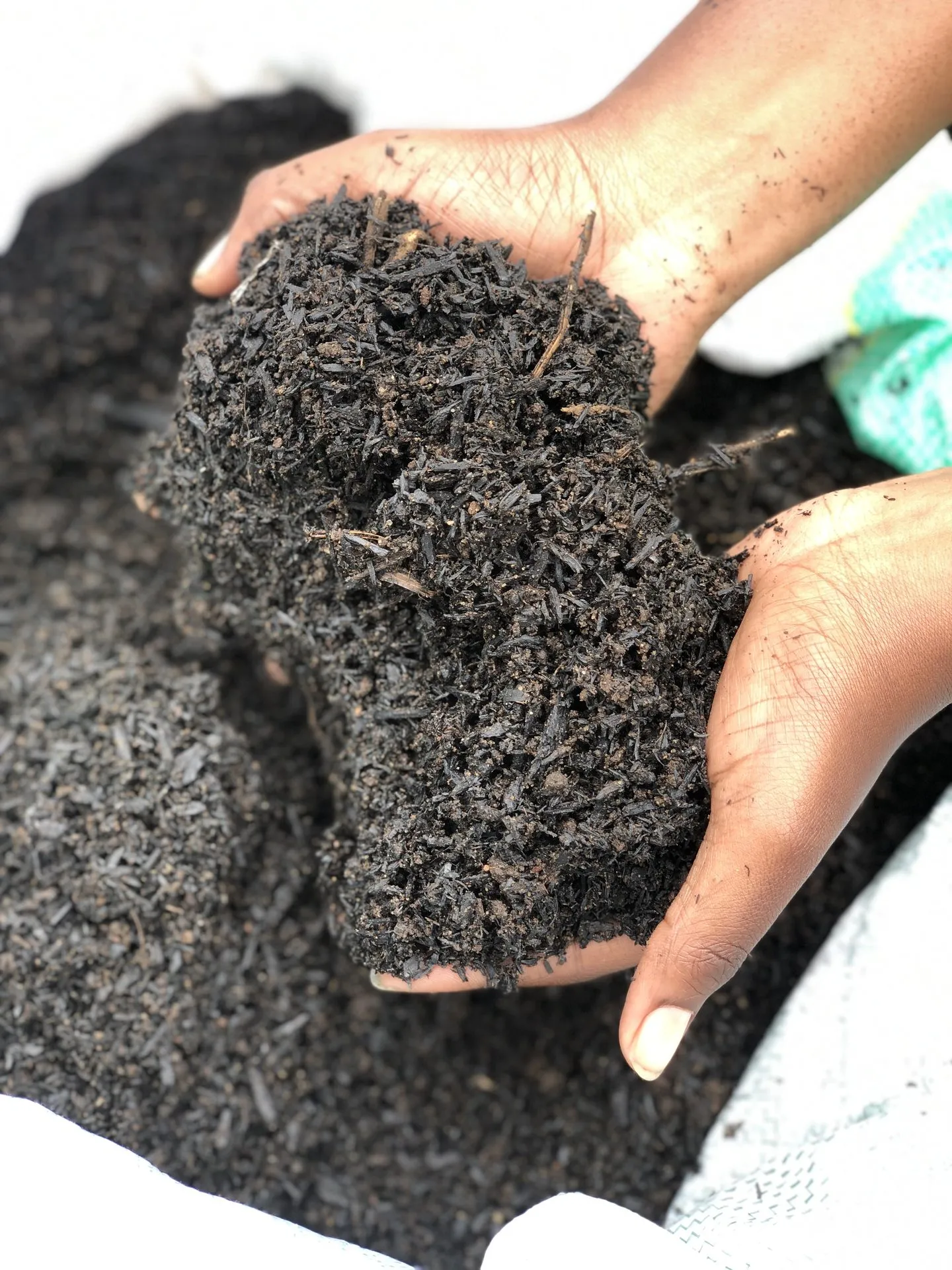 Hands lifting a dark biochar blend out of an open product bag