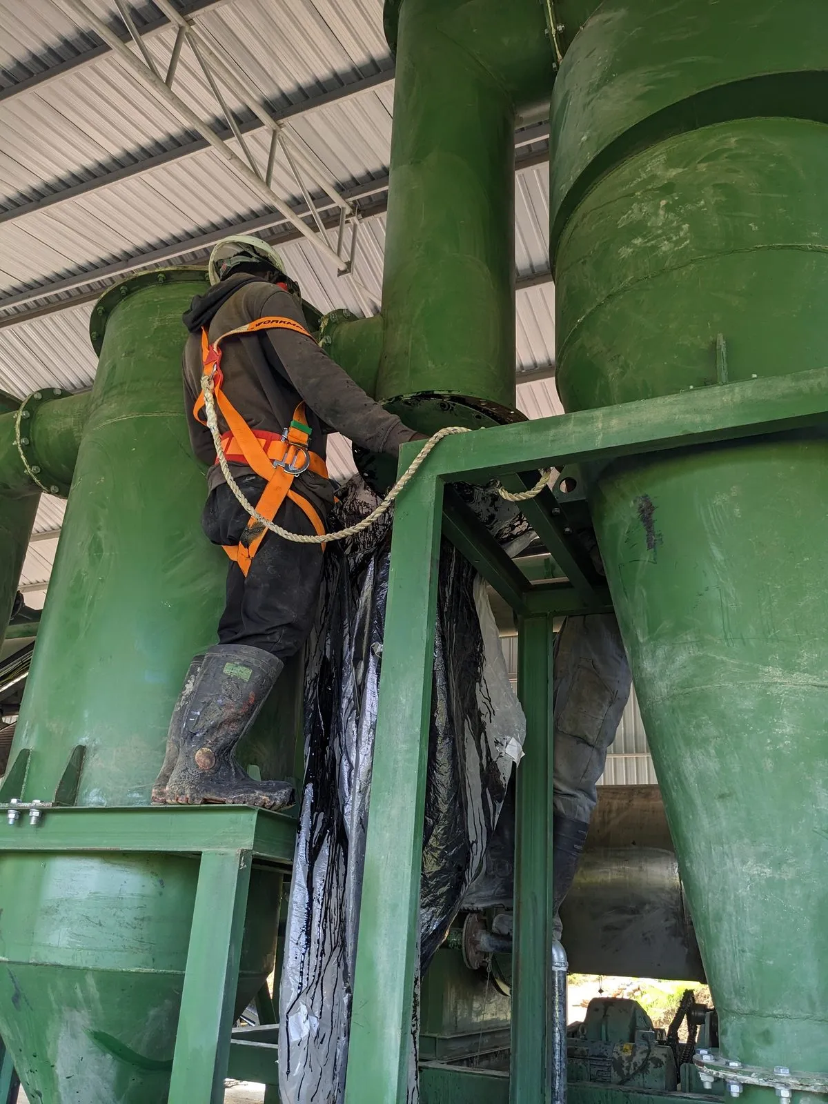 An engineer in a fall-arrest harness working at height on the cyclone assembly